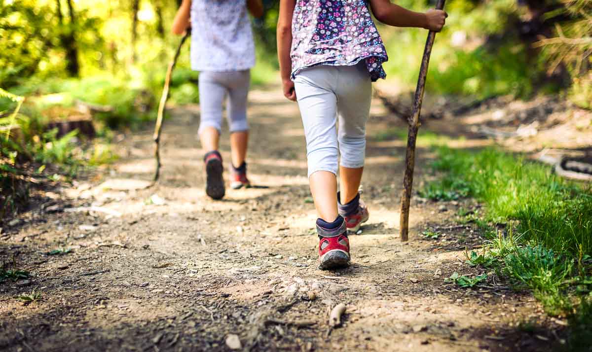 Zwei Mädchen mit Wanderstöcken und Wanderschuhen auf einem Waldweg