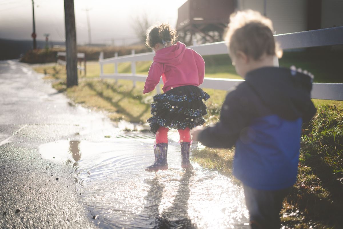 Zwei Kinder springen in Gummistiefeln in eine Pfütze